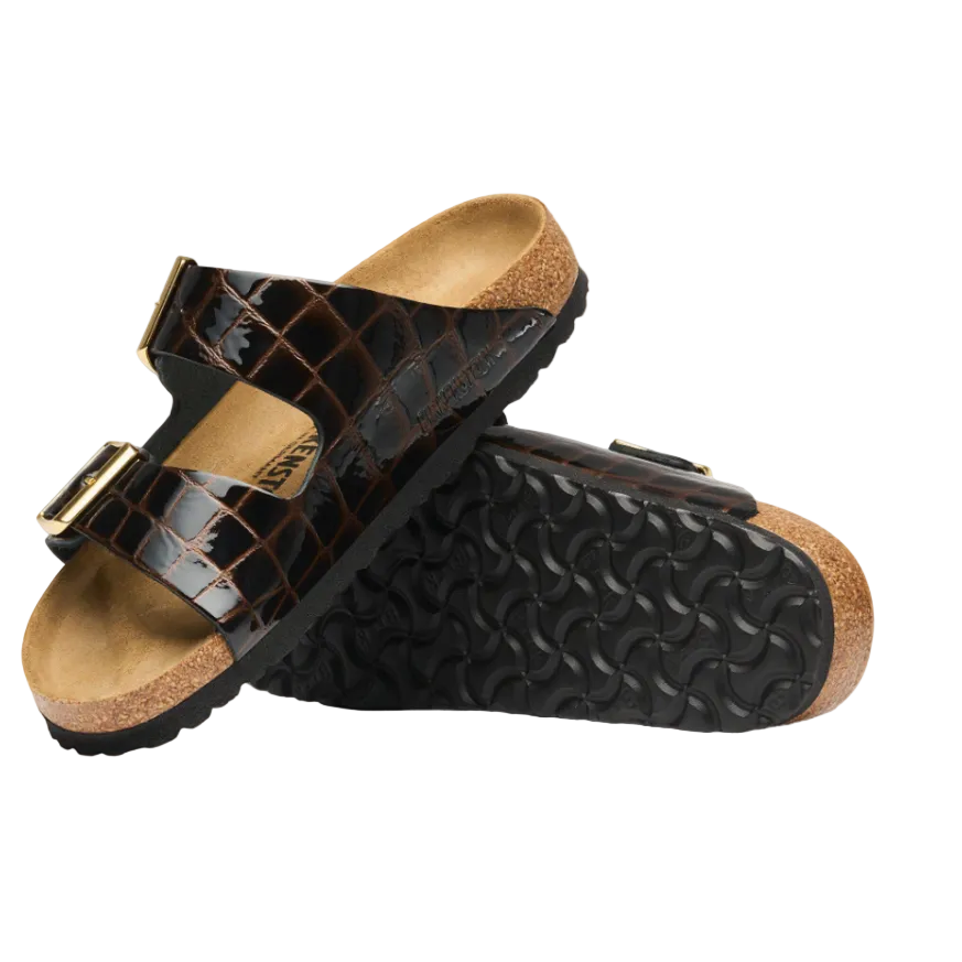 A pair of black crocodile-embossed double-strap slide sandals with gold-tone buckle details and a natural cork footbed and outsole edge, shown on a white background.