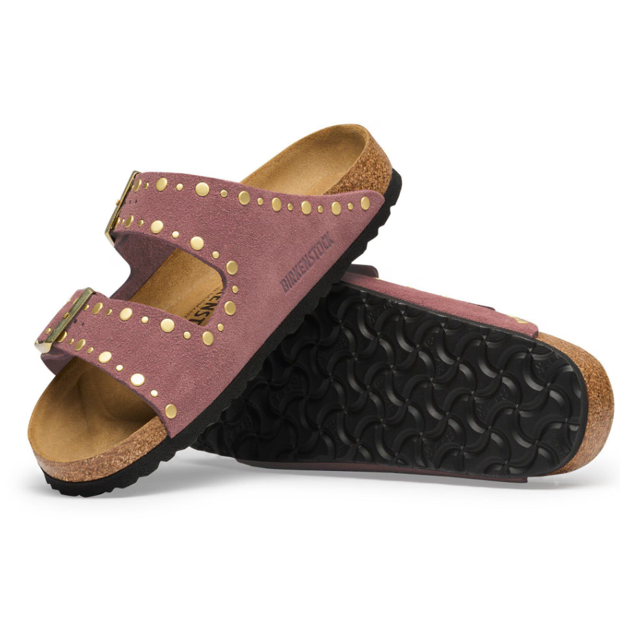 A pair of Birkenstock slide sandals in dusty rose suede with gold-tone metal studs and buckles, featuring a cork footbed and a black textured outsole, shown against a plain white background.