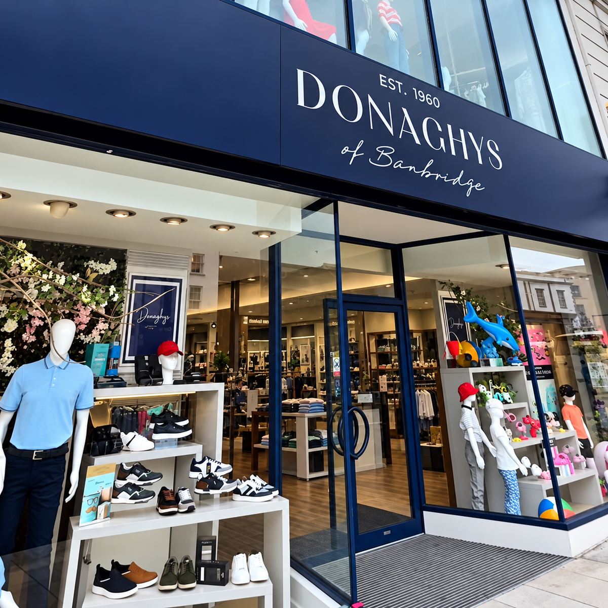 The storefront of Donaghys of Banbridge, featuring a dark navy blue sign and glass entrance. Mannequins and clothing displays are visible outside, and the interior shop is seen through the glass doors.