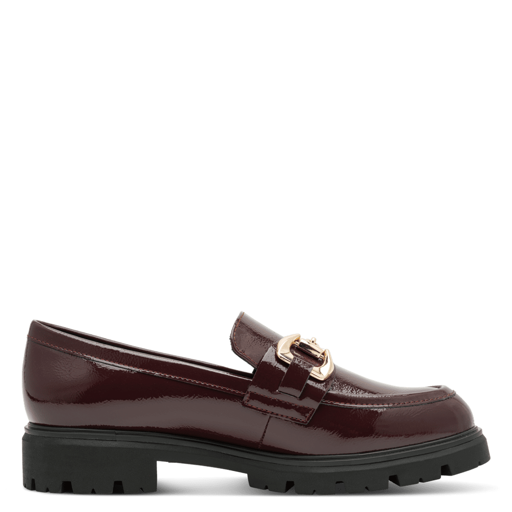 A single burgundy patent leather loafer with a gold-tone horsebit buckle and a chunky black lug sole, shown in profile against a solid green background.