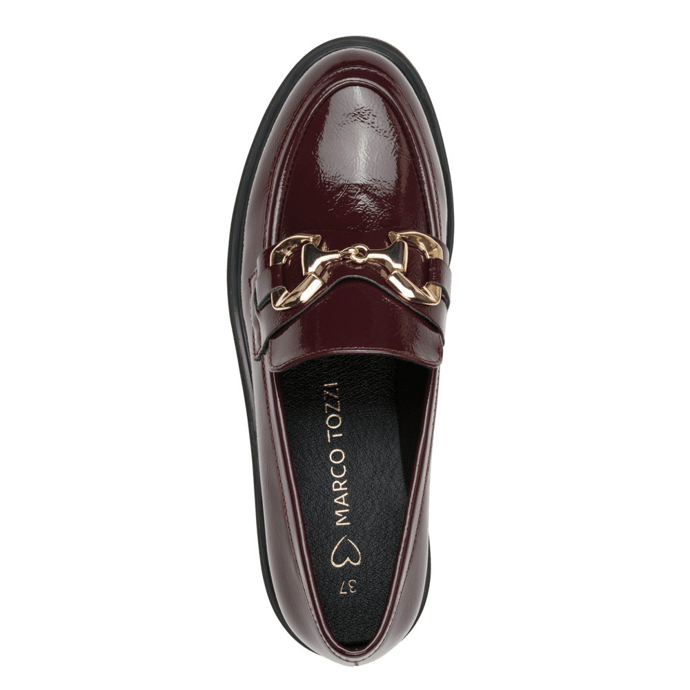 A single dark burgundy patent leather loafer by Marco Tozzi, featuring a gold horsebit detail across the vamp, shown from a top-down view against a solid green background.