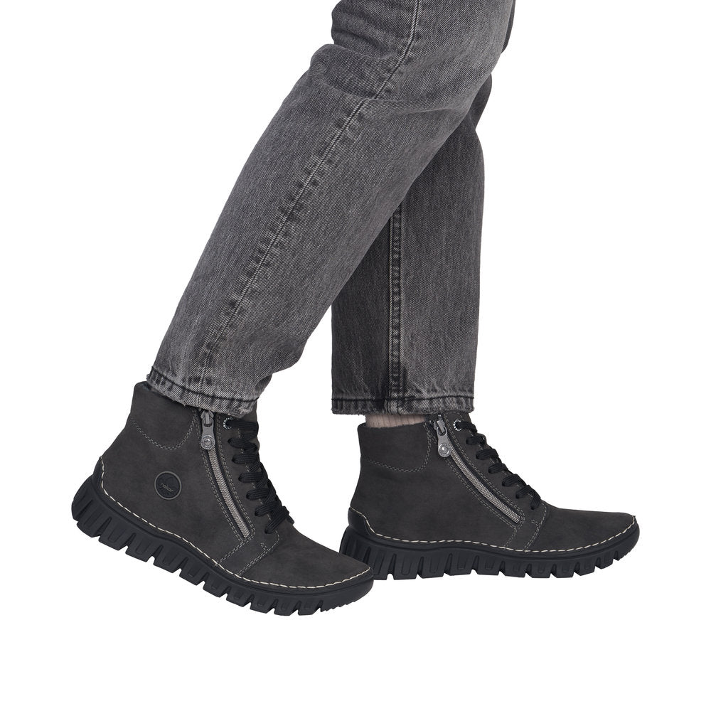 A person wearing dark gray jeans and black ankle boots with side zippers, shown from the knees down against a plain white background.